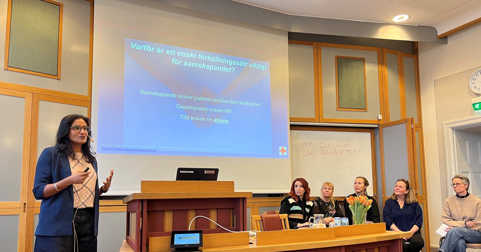 Kvinna håller presentation inför publik, powerpoint med text om etik och samskapande projiceras på väggen bakom.