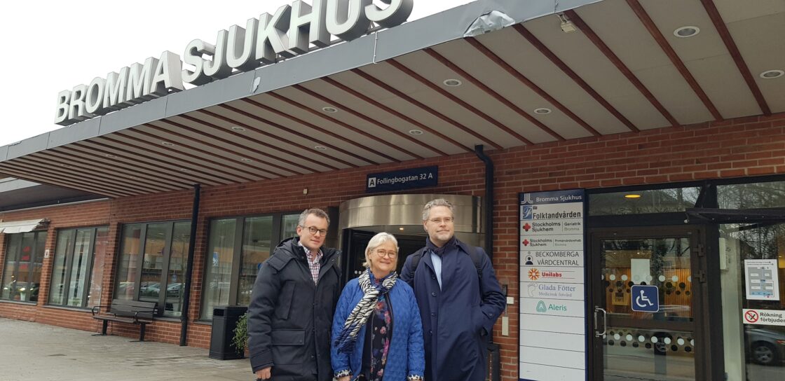 Tre personer står utanför entrén till Bromma Sjukhus under en skylt med sjukhusets namn.