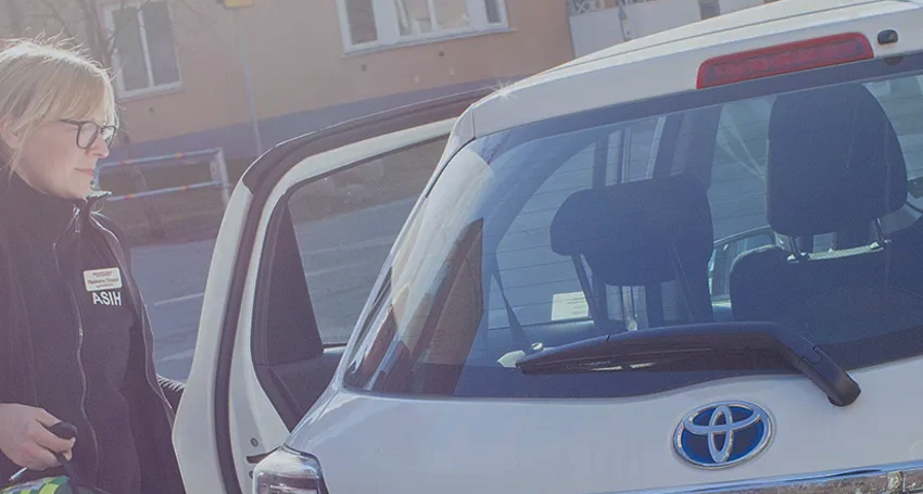 Kvinna med glasögon står vid öppen bildörr, bil av märket Toyota i förgrunden.