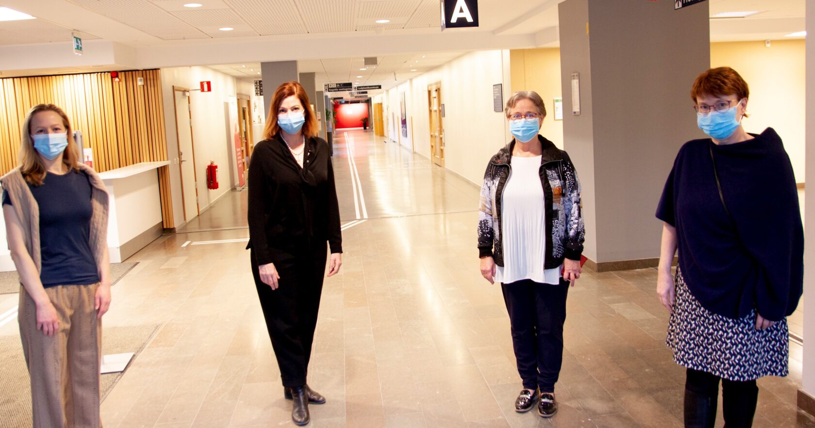 Fyra kvinnor med munskydd står i ett avstånd från varandra i en ljus sjukhuskorridor.