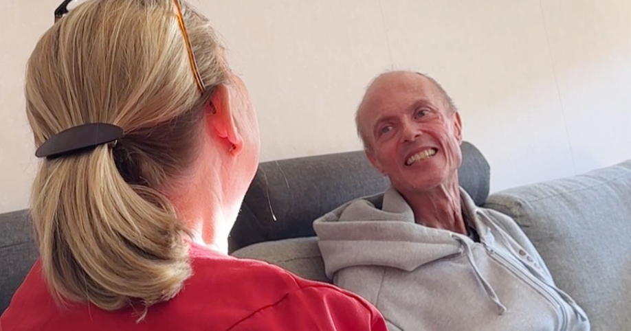 Två personer sitter på en soffa och pratar, den ena ler mot den andra.