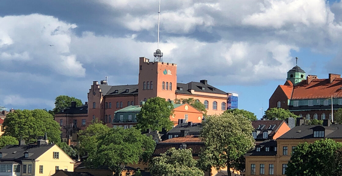 Gamla byggnader och träd under en blå himmel med moln, tagen i ett stadsområde.