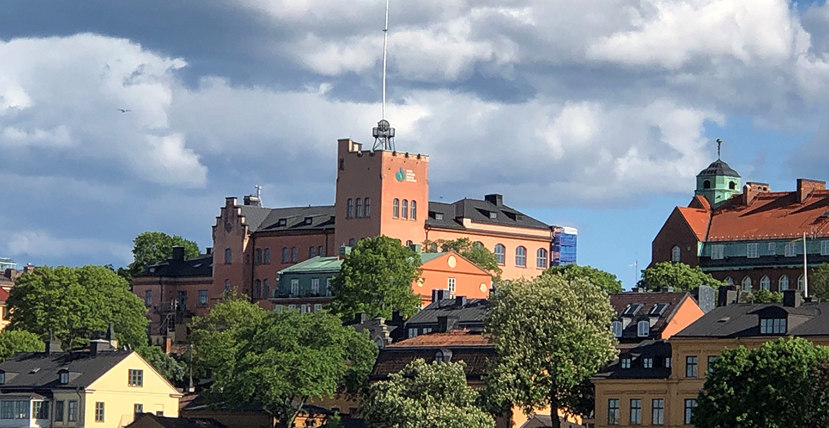 Gamla byggnader och träd under en blå himmel med moln, tagen i ett stadsområde.