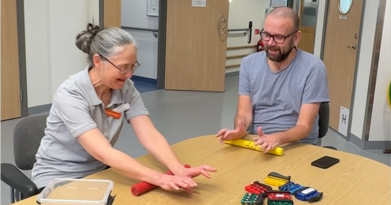 Två vuxna personer sitter vid ett bord med färgglada leksaksbilar och pratar och skrattar tillsammans.