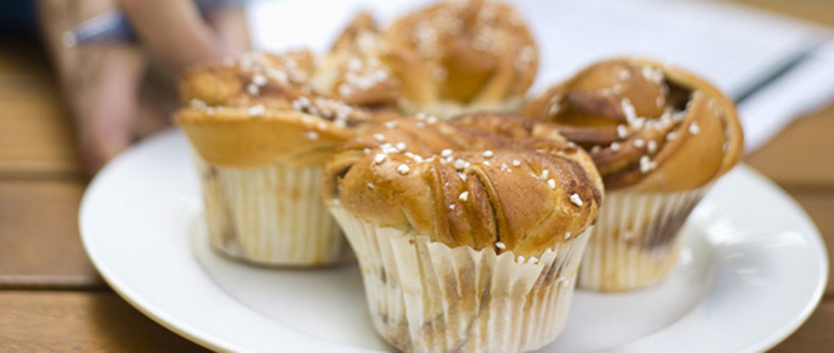 Fyra kanelbullar med pärlsocker på en vit tallrik.