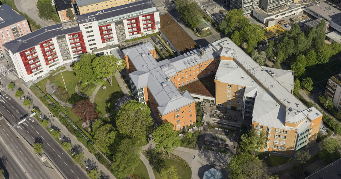 Fågelvy över bostadshus och grönområden i stadsmiljö med vägar och träd runt byggnaderna.
