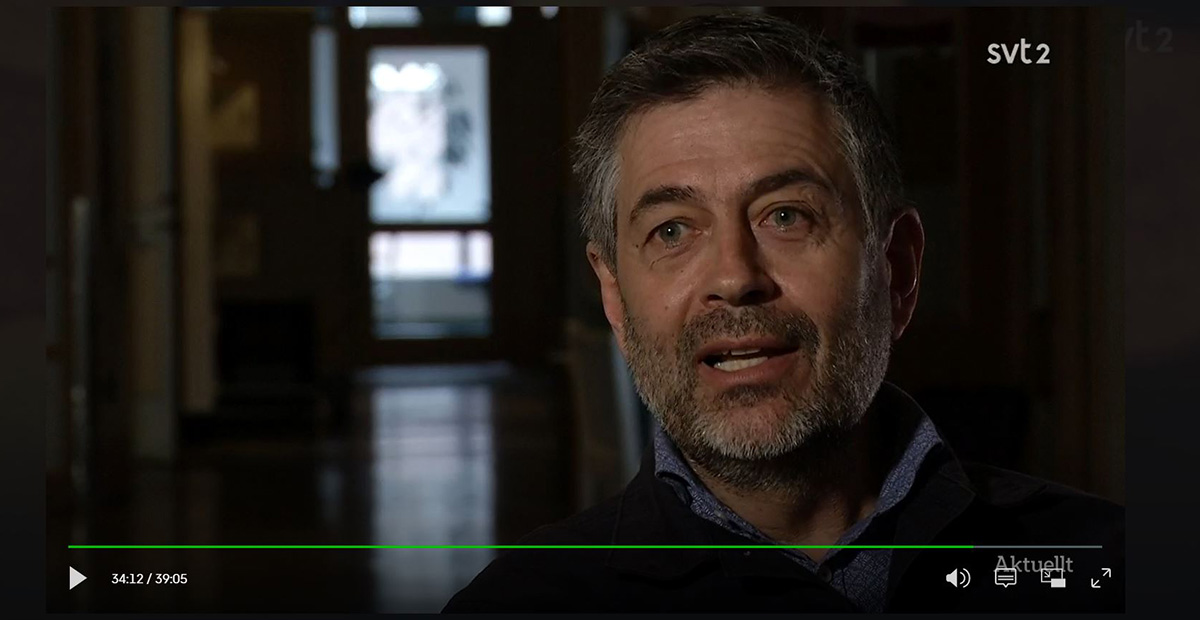 Man med grått hår och skägg intervjuas i mörkt rum, SVT2-logga syns, text "Aktuellt" nere till höger.