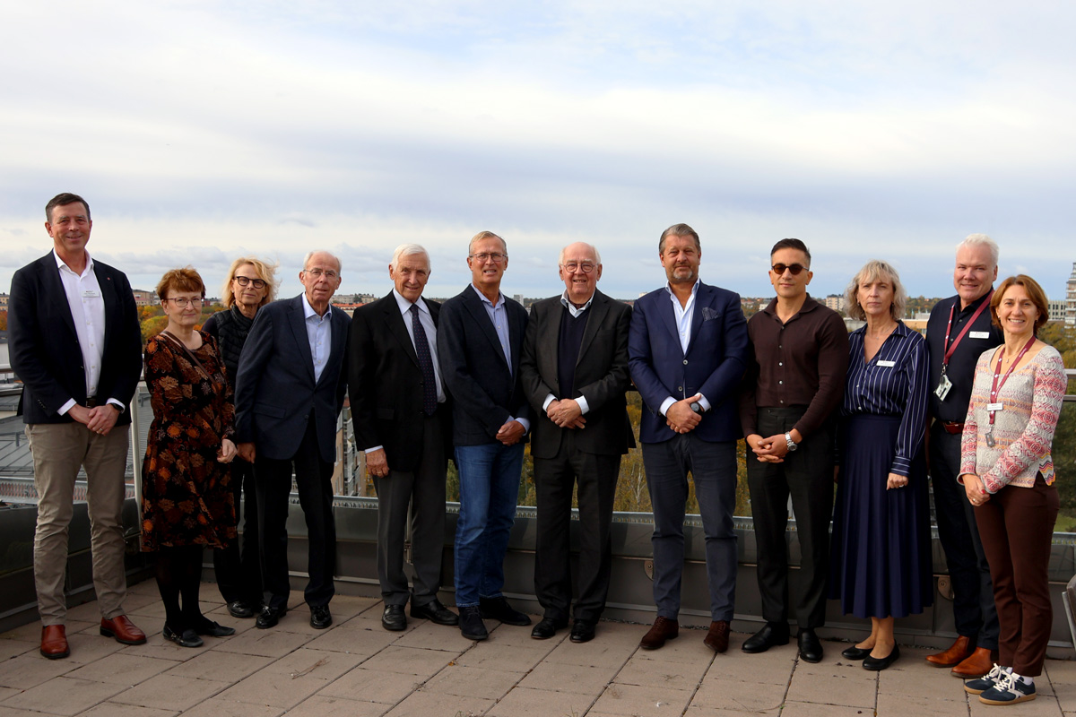 Gruppfoto på tolv personer stående utomhus på en takterrass med stad i bakgrunden.