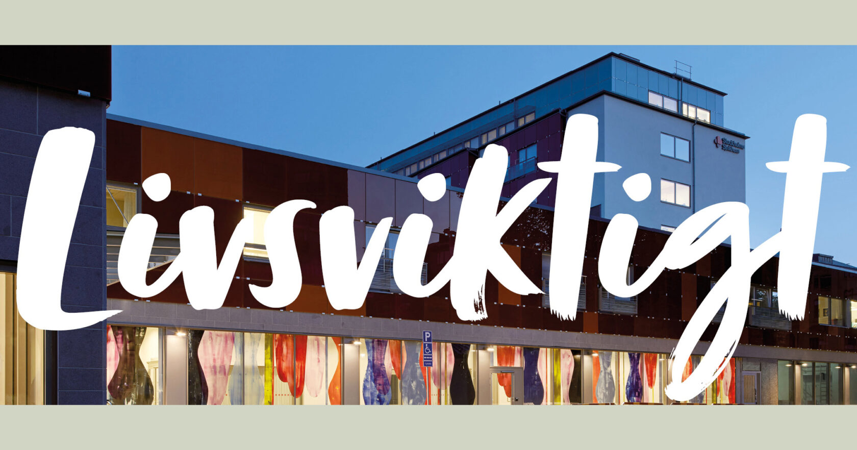 Sjukhusbyggnad i skymning med färgglada fönster och texten "Livsviktigt" i stora vita bokstäver.