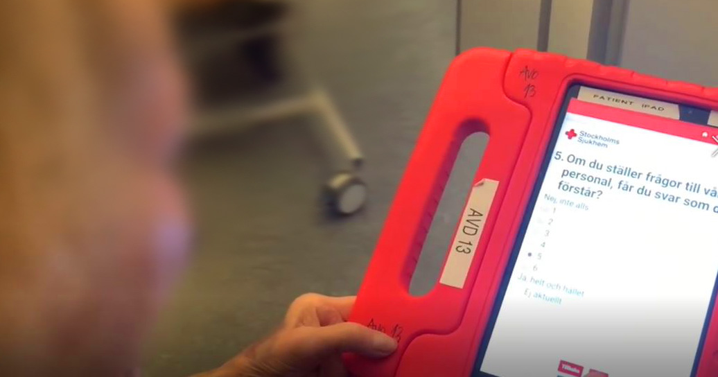 Person håller en surfplatta med rött fodral och fyller i en digital enkät från Stockholms Sjukhem.