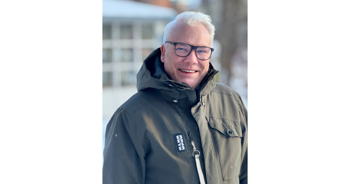 Man med glasögon och vinterjacka står utomhus i snöigt landskap och ler mot kameran.