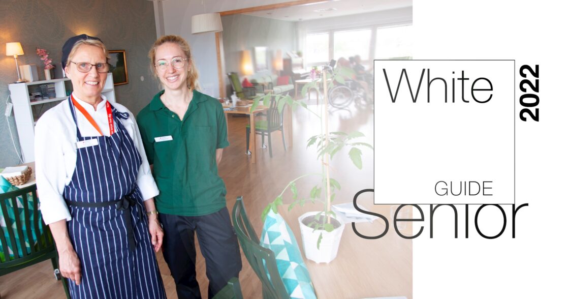 Två kvinnor, en i kökskläder och en i grönt, står i ett ljust äldreboende. Text: White Guide Senior 2022.