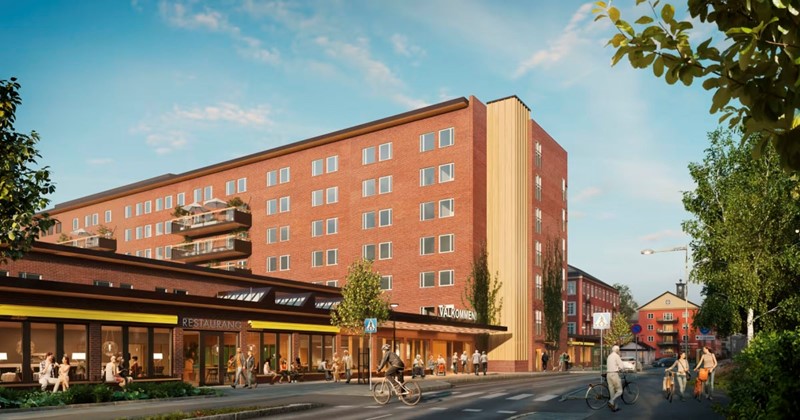 Röd tegelbyggnad med butiker och restaurang i bottenplan, människor och cyklister på gatan utanför.
