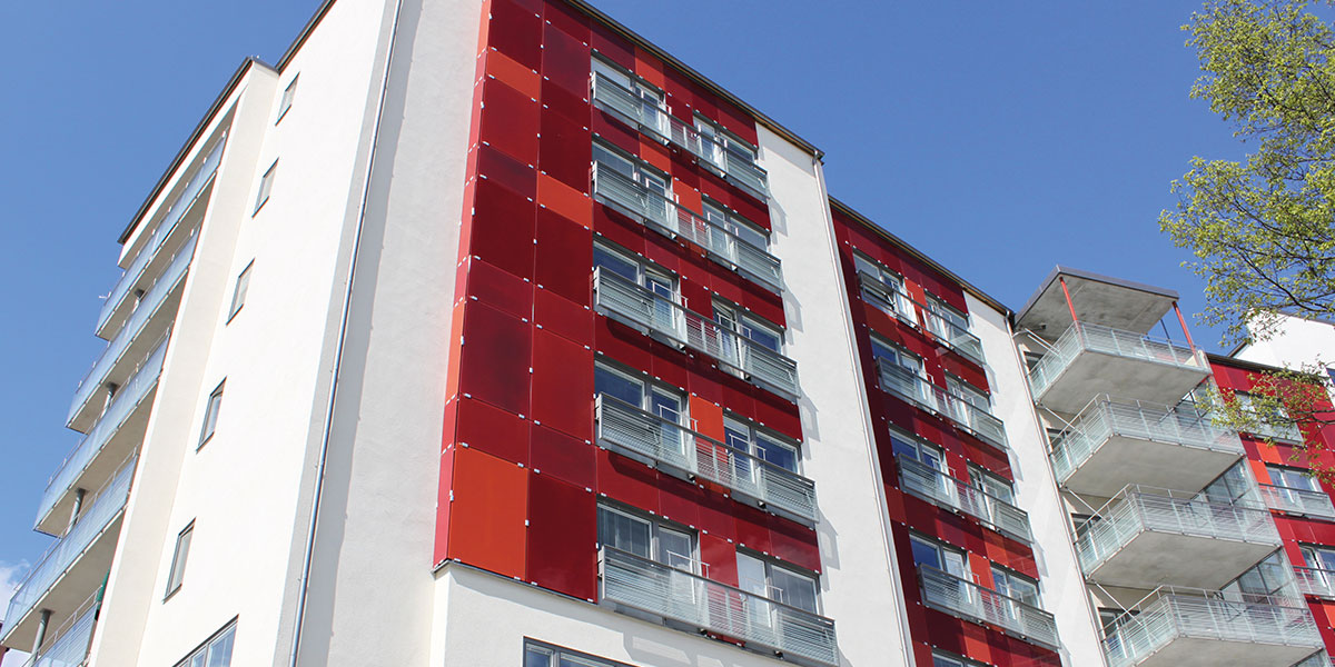 Modernt flerbostadshus med vita väggar, röda paneler och balkonger mot blå himmel.