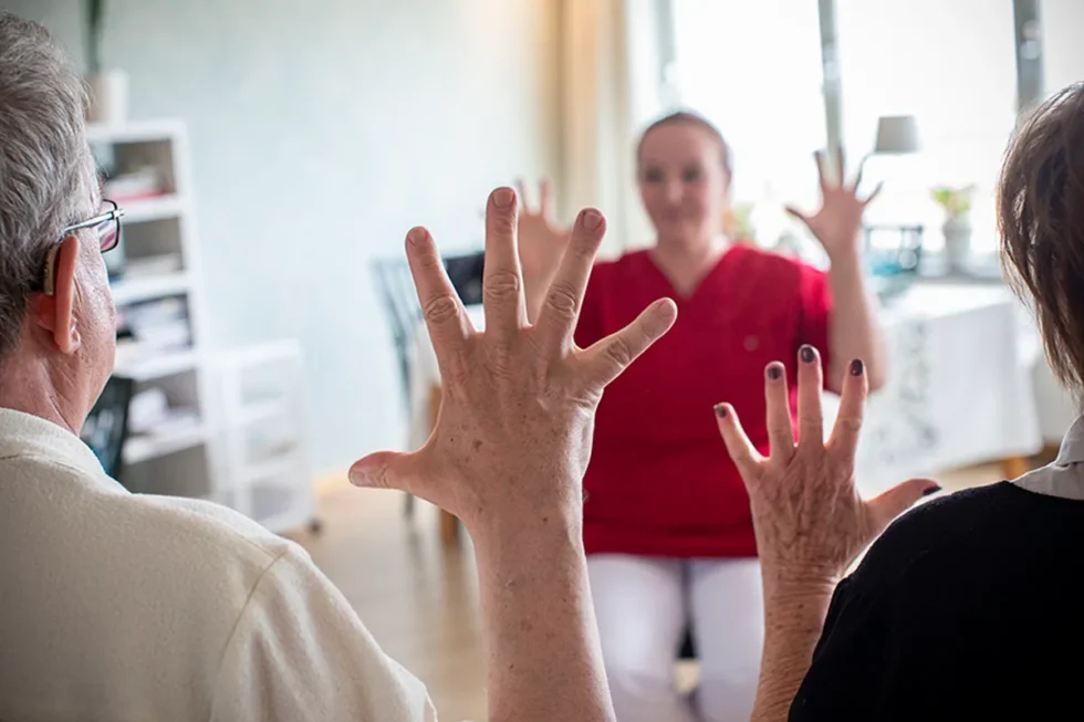 En medarbetare gör handgymnastik. Två boende syns som gör handgymnastiken tillsammans med medarbetaren.