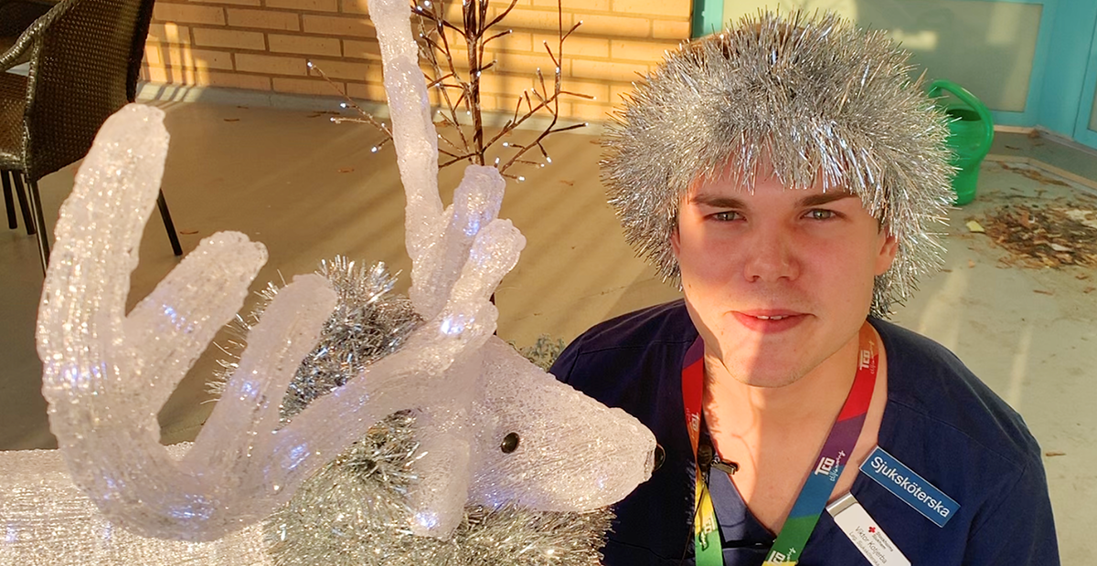 En person med glitterperuk bredvid en glittrande dekorationsren på en uteplats i solsken.
