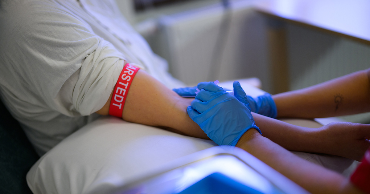 Sjuksköterska i blå handskar förbereder blodprov på persons arm med stasband.