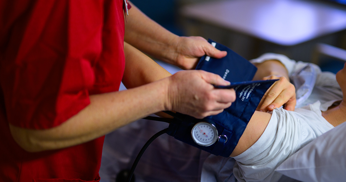 Sjukvårdspersonal i röd uniform tar blodtryck på en patient som ligger ner.